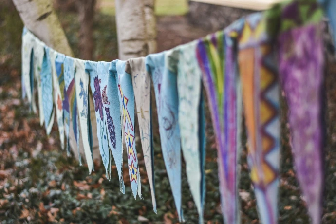 Colorful fabric bunting hangs between trees outdoors.